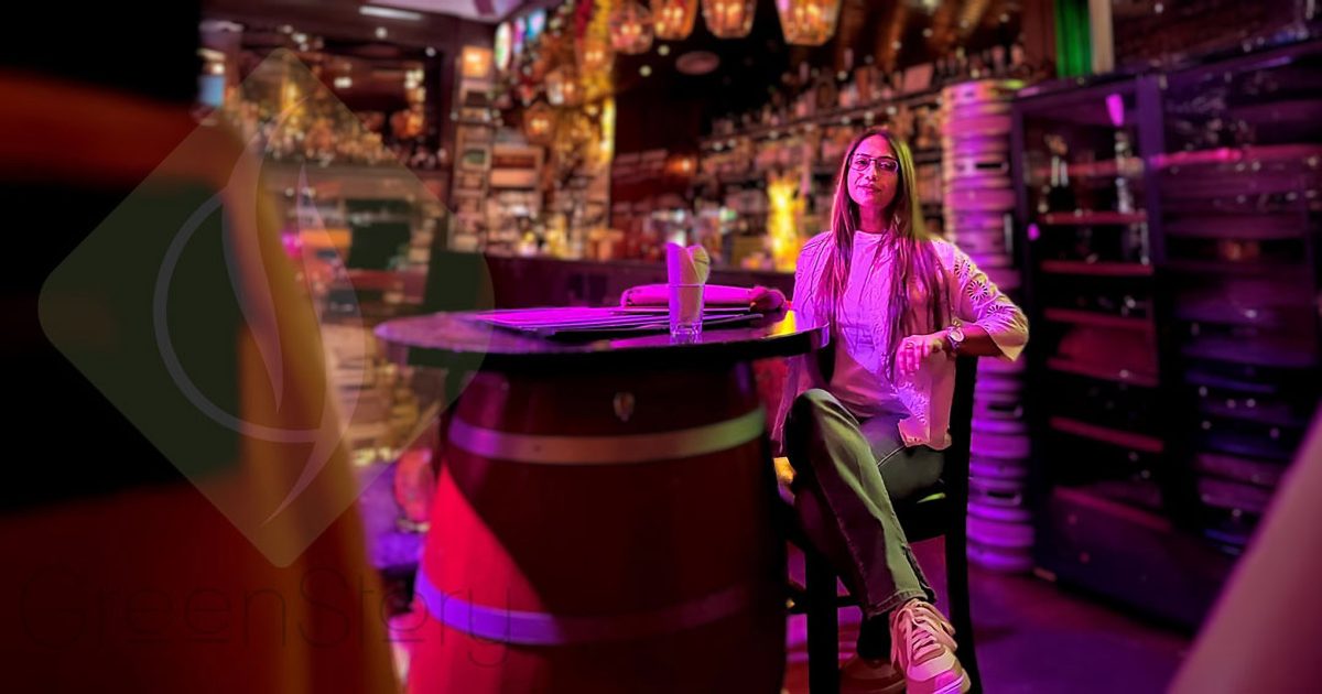 A woman relaxing at a vibrant, eco-friendly Malaysian bar with colorful lighting and sustainable decor.